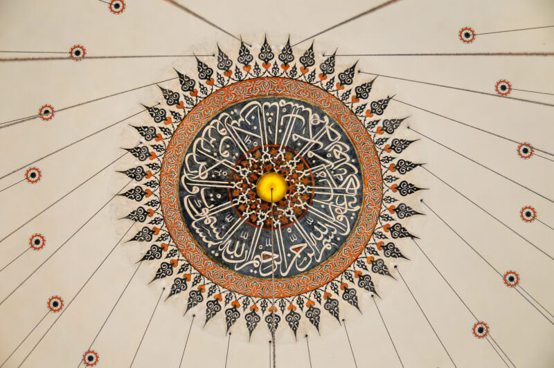 Painted calligraphic medallion at the apex of Rustem Pasha Mosque's dome with radiating ornament and lamp wires
