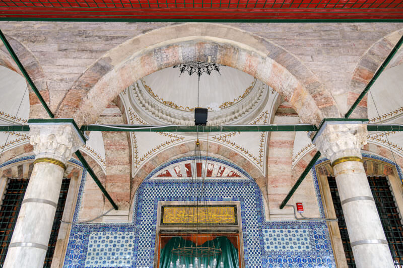 Painted arches and tiled walls framing the entrance dome and gilded calligraphic panel of Rustem Pasha Mosque