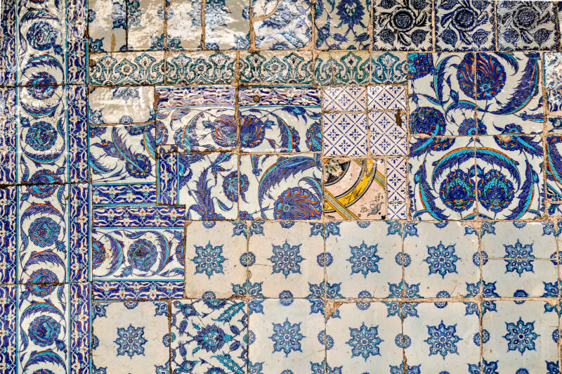 Weathered Iznik tile panels on Rustem Pasha Mosque's exterior showing mismatched tulip and rosette patterns in blue and turquoise