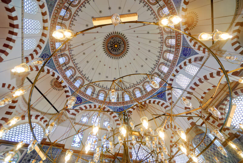 Low-hanging chandeliers beneath Rustem Pasha Mosque's painted dome with its calligraphic medallion and arched windows