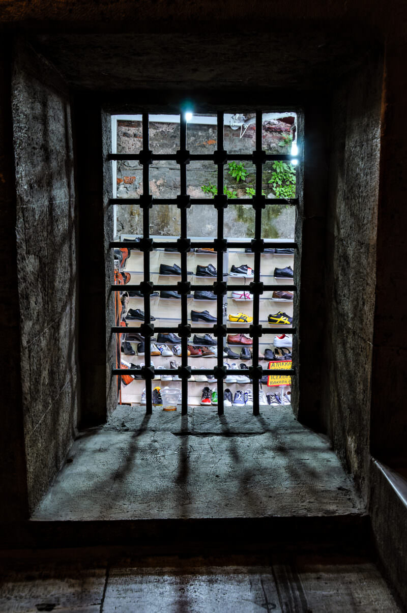 Shoe stall shelves seen through an iron grille beneath the raised platform of Rustem Pasha Mosque