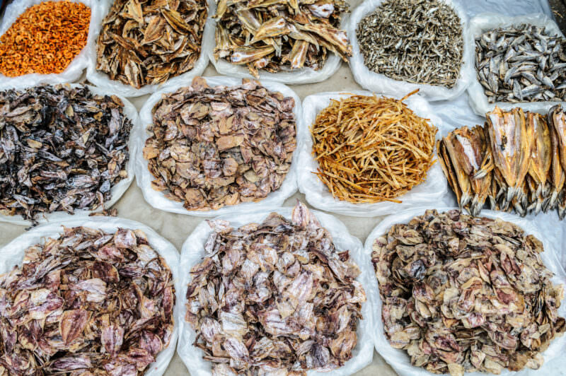 Dried squid, shrimp, and split fish sorted into plastic-lined piles, brown and gold tones against white trays
