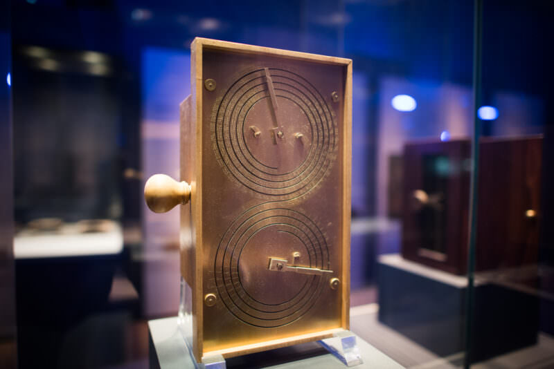 Michael Wright reconstruction model showing spiral dial mechanism through transparent case, bronze-toned metalwork in a museum display