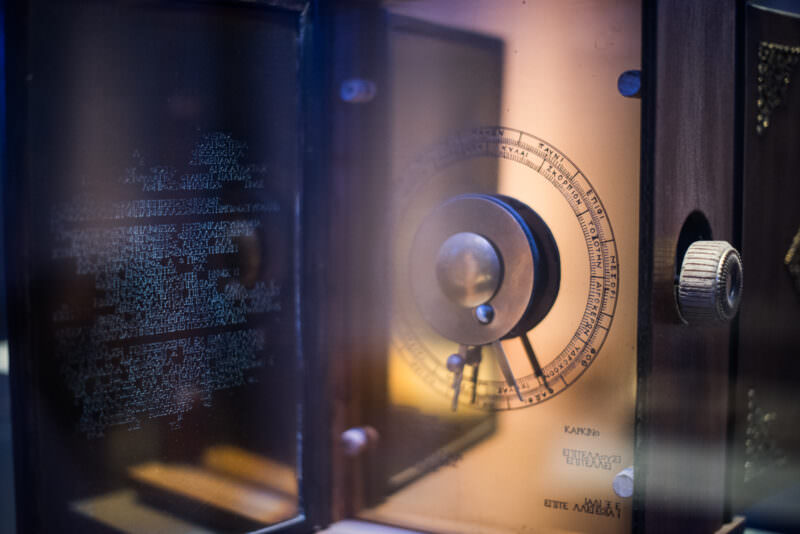 Modern Antikythera Mechanism reconstruction in brass with circular dials and Greek text inscriptions, displayed on a clear stand
