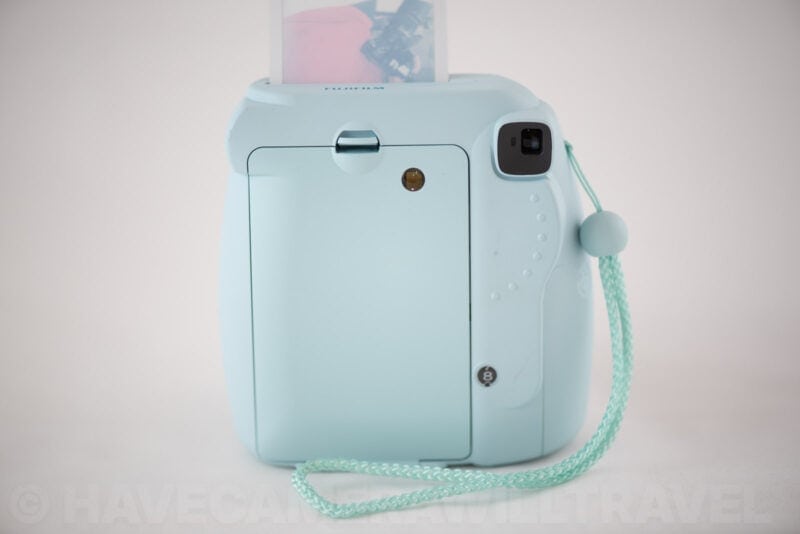 Back of the Instax Mini 8 with its film door open and a printed photo ejecting from the top slot