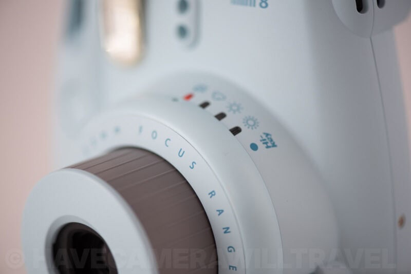 Close-up of the Instax Mini 8's exposure options dial encircling its ridged lens barrel