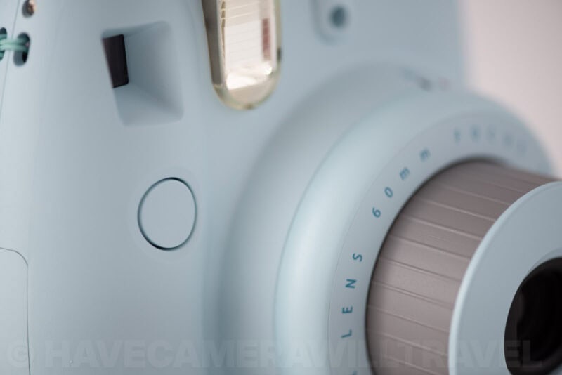 Close-up of the Instax Mini 8's round shutter button beside its 60mm lens ring