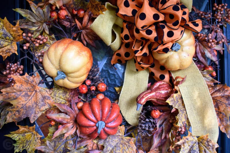Autumn wreath decorated with faux pumpkins, berries and a polka-dot orange bow
