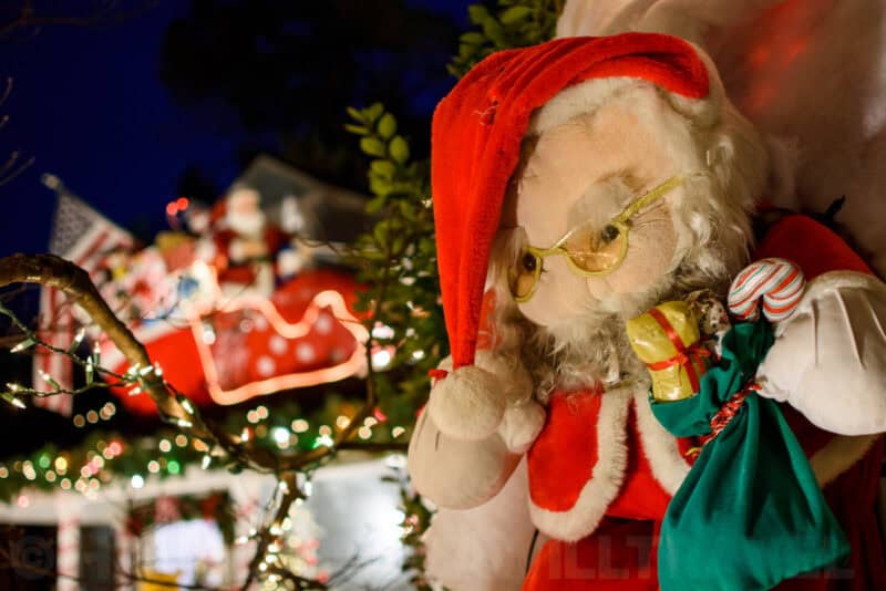 Close-up of a plush Santa Claus figure with a sleigh and lights on a decorated house roof
