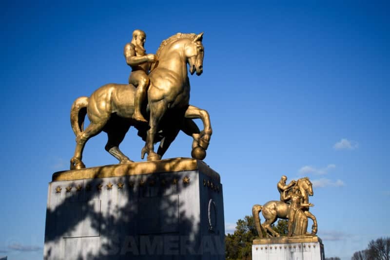 Golden equestrian statues atop pedestals at Arlington Memorial Bridge under a clear blue sky
