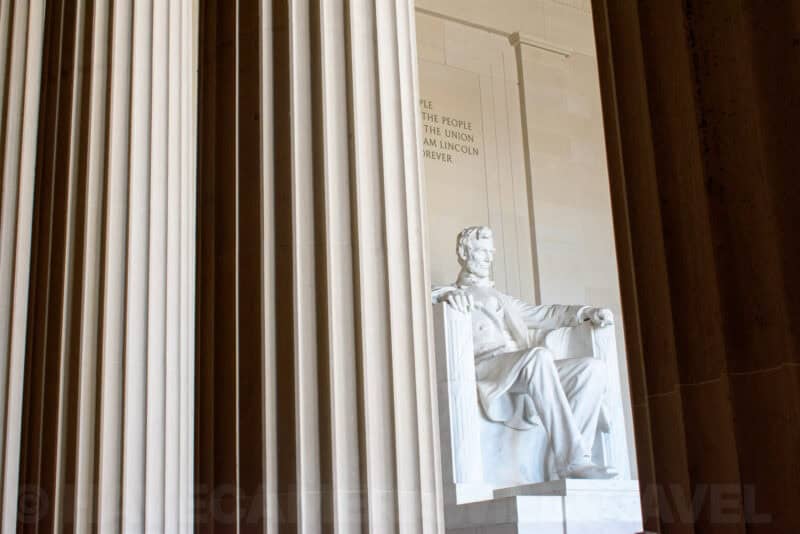 Lincoln Memorial statue framed between marble columns with inscribed wall text visible