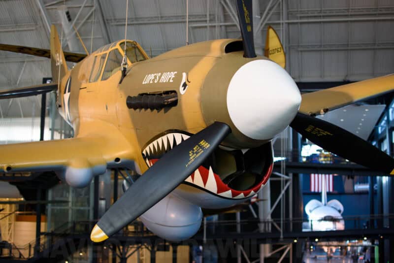 Curtiss P-40 Warhawk fighter plane with shark-mouth nose art hanging in a museum gallery