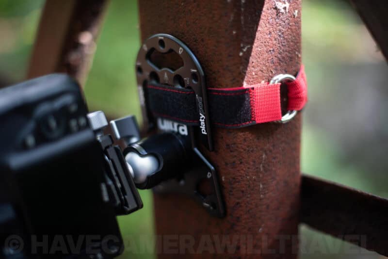Platypod Ultra secured to a rusty metal post with its strap, holding a mirrorless camera