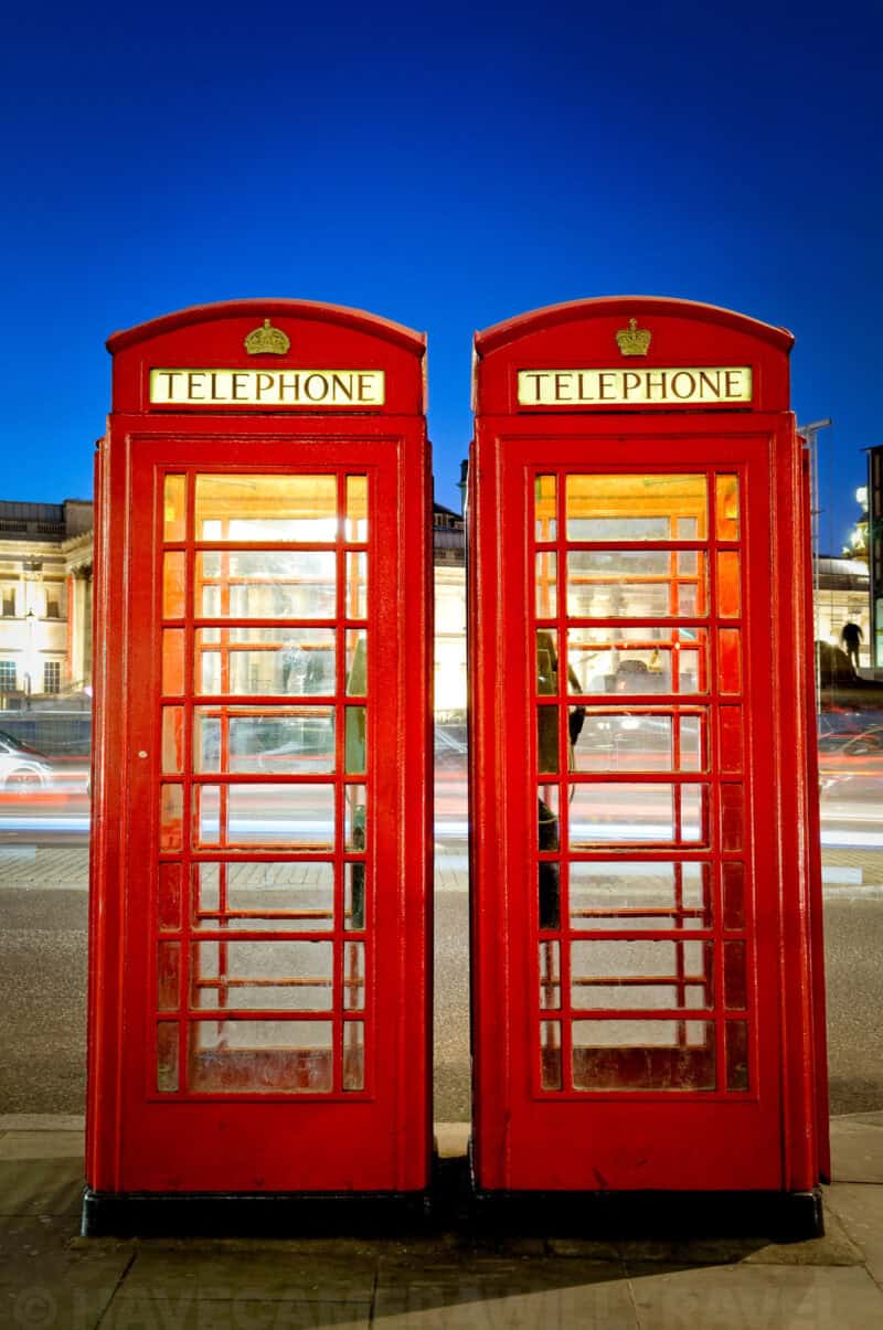 Twin red British telephone boxes glowing at dusk with light-trailed traffic behind them