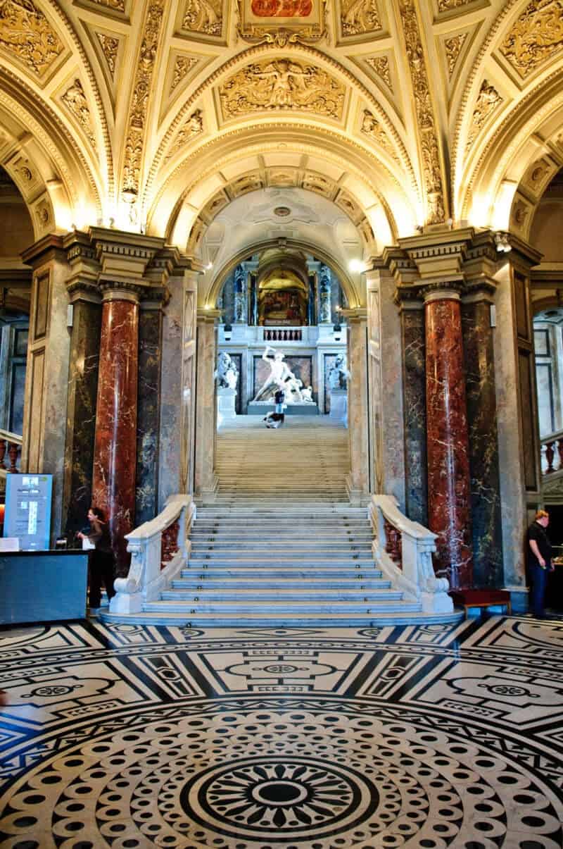 Grand marble staircase beneath an ornately gilded arched ceiling inside a Brussels museum