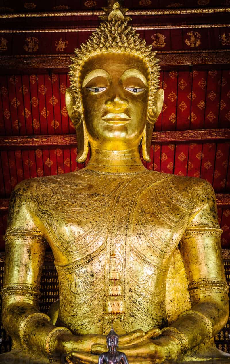 Close-up of a large gilded Buddha statue inside a dimly lit pagoda in Luang Prabang