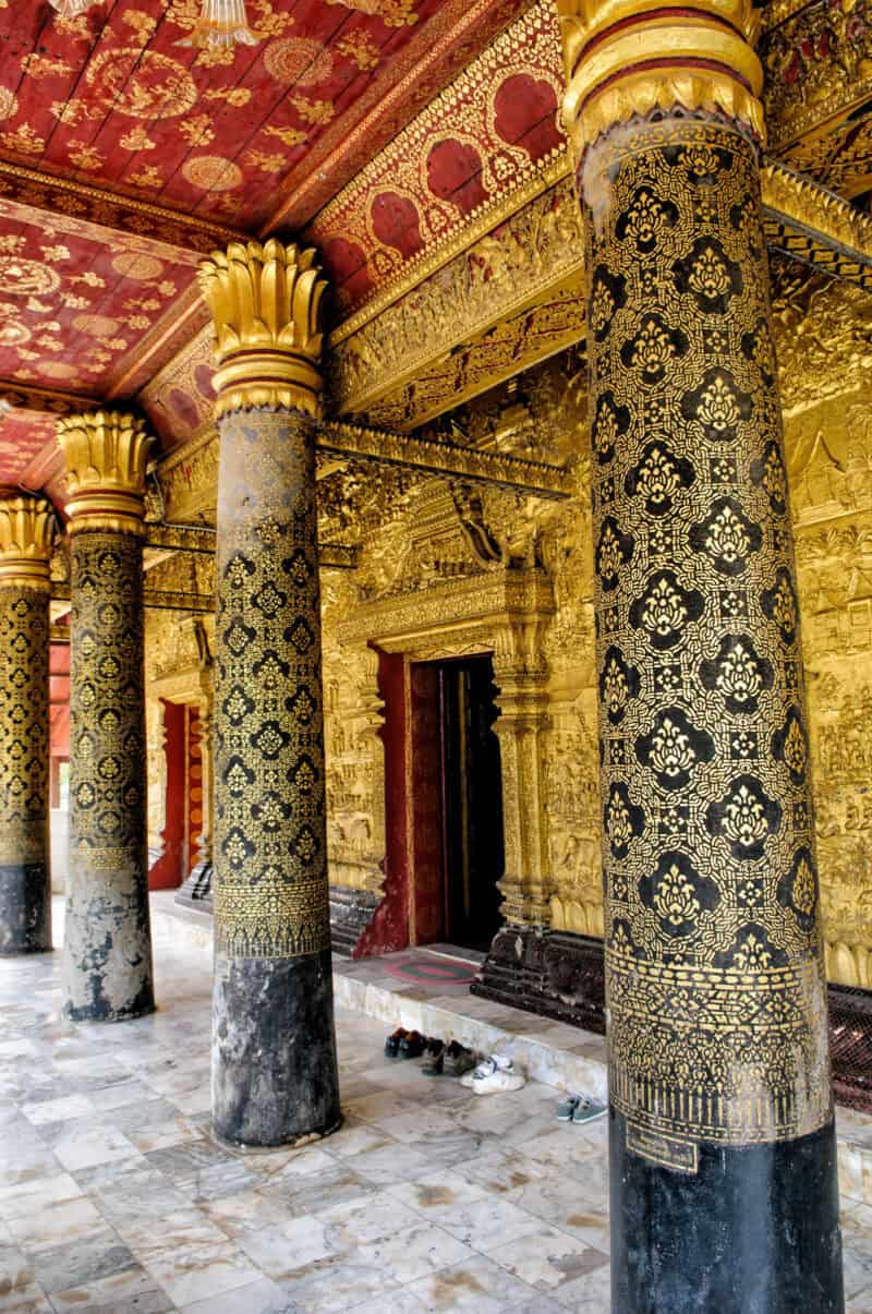 Ornate gilded columns and painted red ceiling along a temple corridor in Luang Prabang