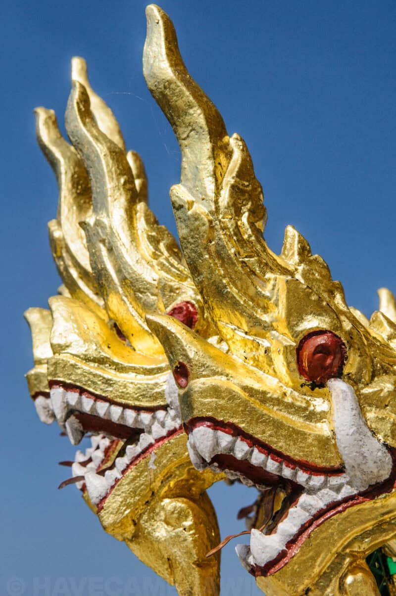 Gilded naga serpent heads carved atop a temple roof against a clear blue sky