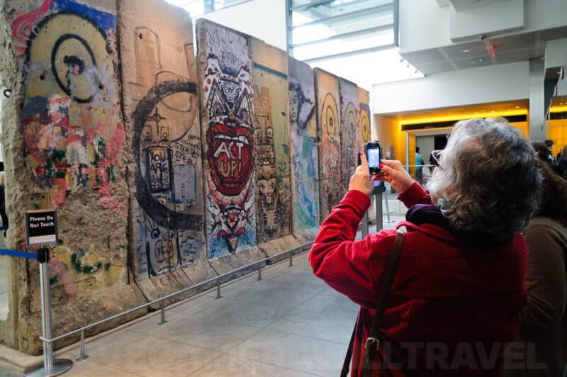 Visitor photographing graffiti-covered Berlin Wall segments displayed indoors at the Newseum
