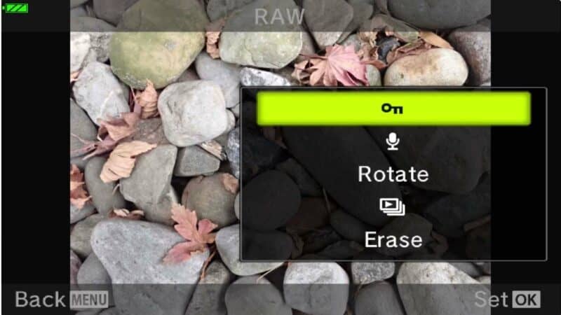 Olympus TG-5 playback menu showing Protect key icon, Rotate, and Erase options over a rocky beach photo