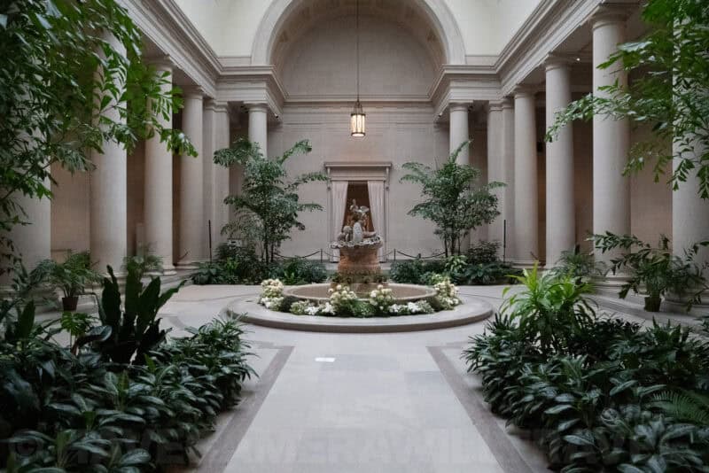 Colonnaded museum courtyard with a central fountain surrounded by lush potted palms
