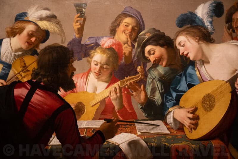 Old master painting of musicians and revelers gathered around a table with lutes and a wine glass