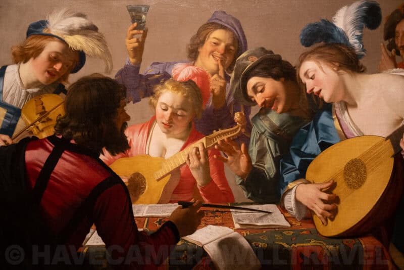 Old master painting of musicians and revelers gathered around a table with lutes and a wine glass