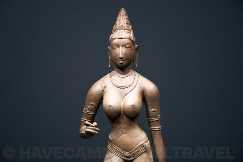 Bronze statue of a South Asian goddess figure lit against a dark museum backdrop