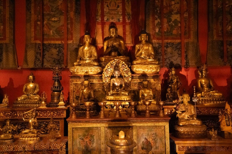 Golden Buddhist statues and shrine objects displayed against a red-walled temple room