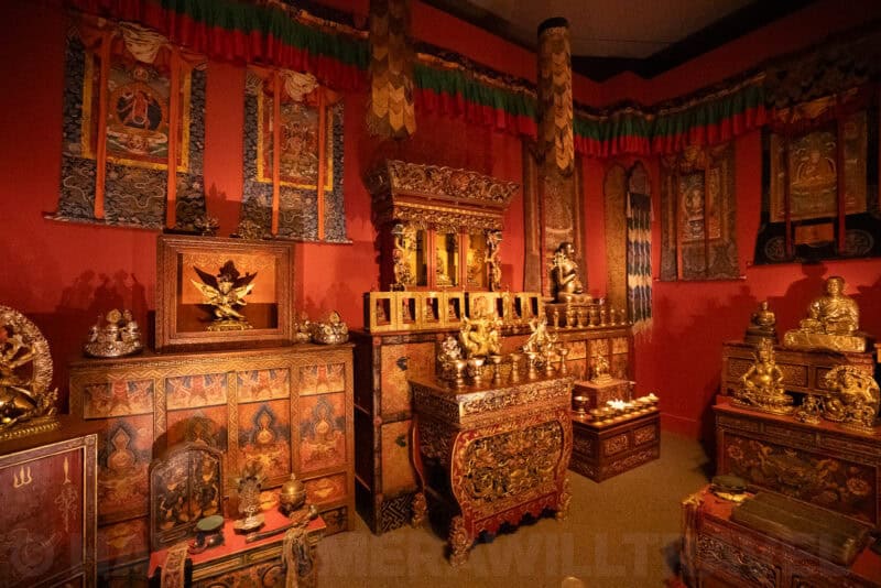 Red Buddhist shrine room with gilded cabinets, statues and hanging thangka paintings