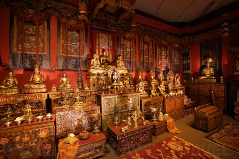 Golden Buddhist statues and shrine objects displayed against a red-walled temple room