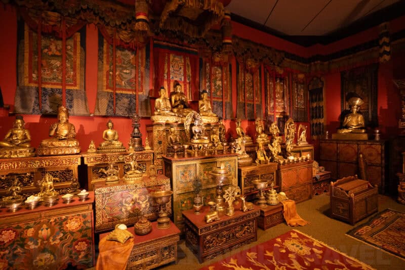 Golden Buddhist statues and shrine objects displayed against a red-walled temple room