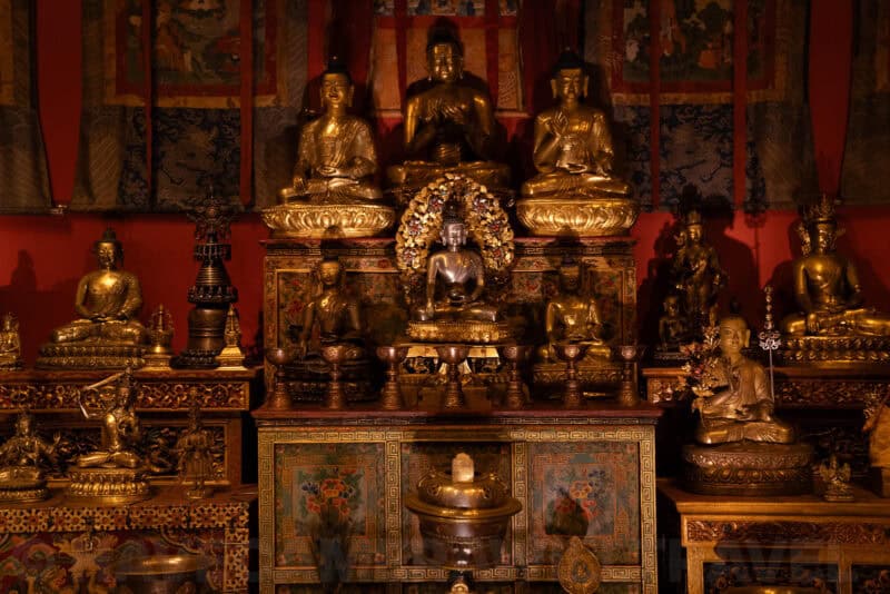 Golden Buddhist statues and shrine objects displayed against a red-walled temple room