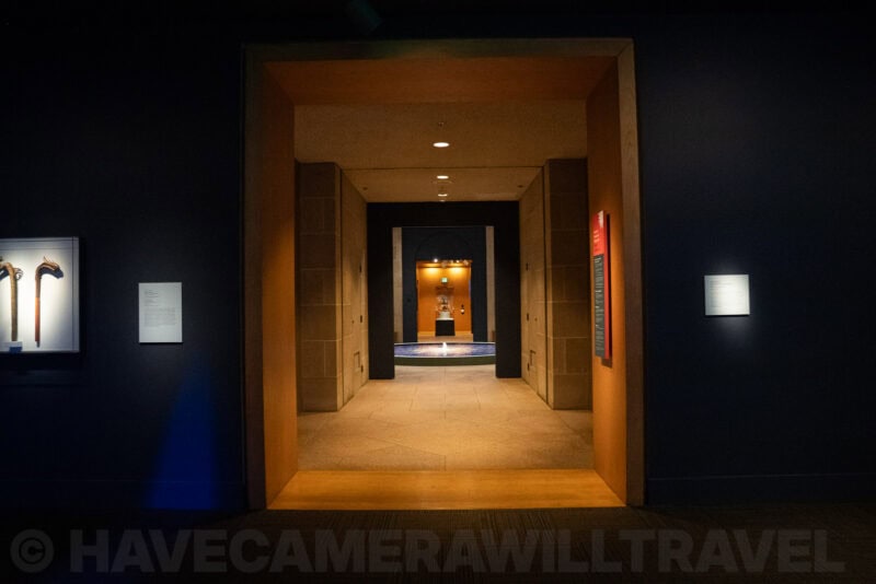 Illuminated museum corridor leading toward a distant sculpture and reflecting pool