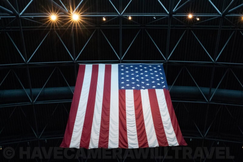 Large American flag hanging inside a geodesic dome structure lit by overhead spotlights
