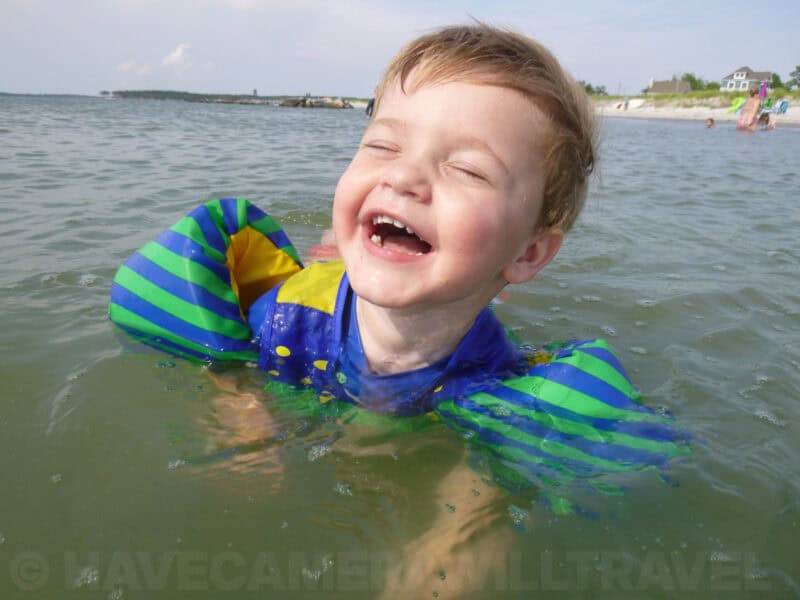 Smiling toddler in green and blue arm floats laughing while swimming in the sea