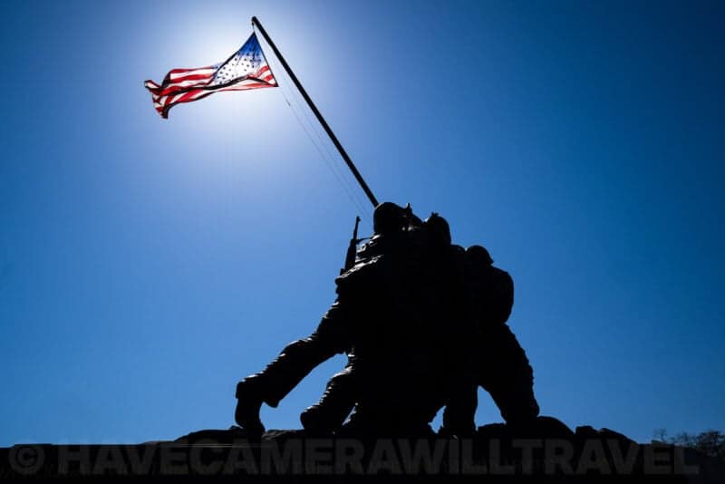 Iwo Jima Memorial statue in silhouette against a blue sky with the American flag flying above