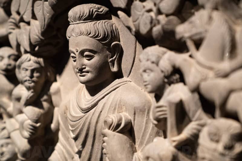 Close-up of a carved stone relief sculpture depicting a serene robed figure among other figures