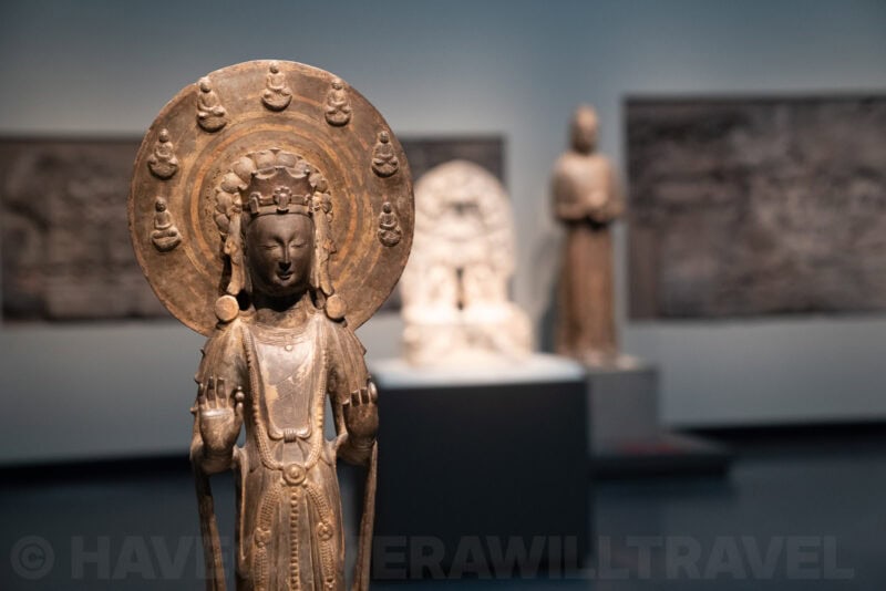 Ancient bronze bodhisattva statue with a halo crown displayed among museum sculptures