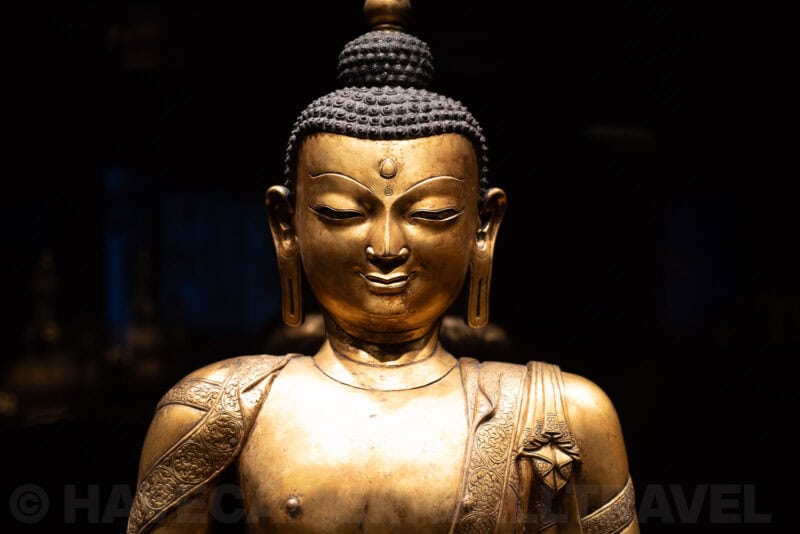 Gilded bronze Buddha statue head and shoulders lit dramatically against a dark background