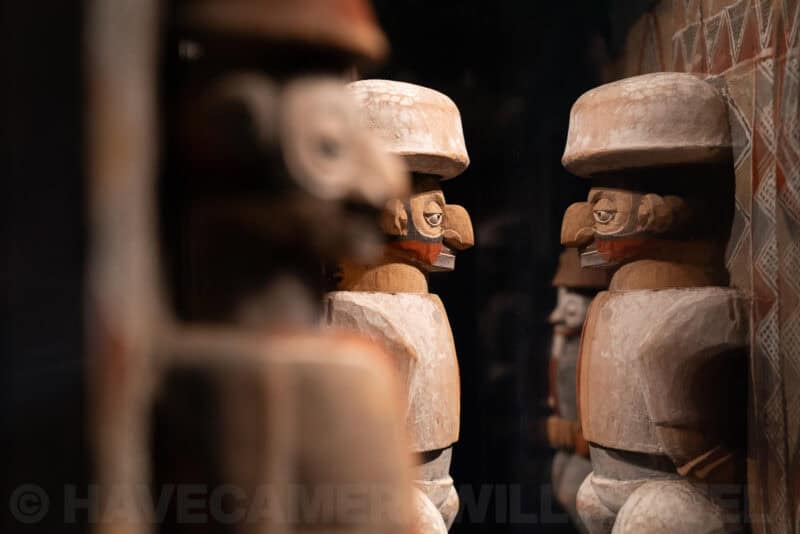 Carved wooden figurines with painted faces displayed on a shelf, foreground blurred