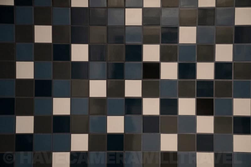 Close-up of glossy square wall tiles in navy, cream, and charcoal forming a checkered mosaic