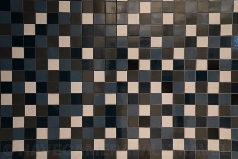 Grid of glossy square wall tiles in navy, cream, and charcoal tones arranged in a mosaic pattern
