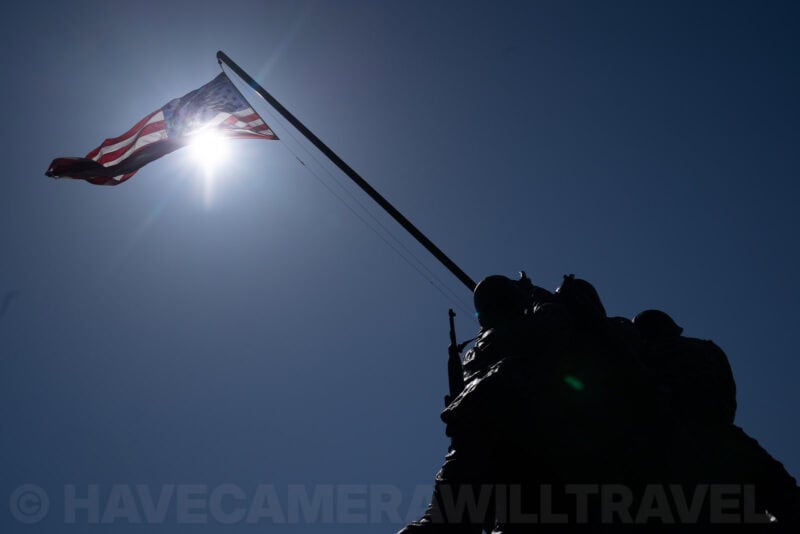 Iwo Jima Memorial statue silhouetted beneath a backlit American flag with lens flare