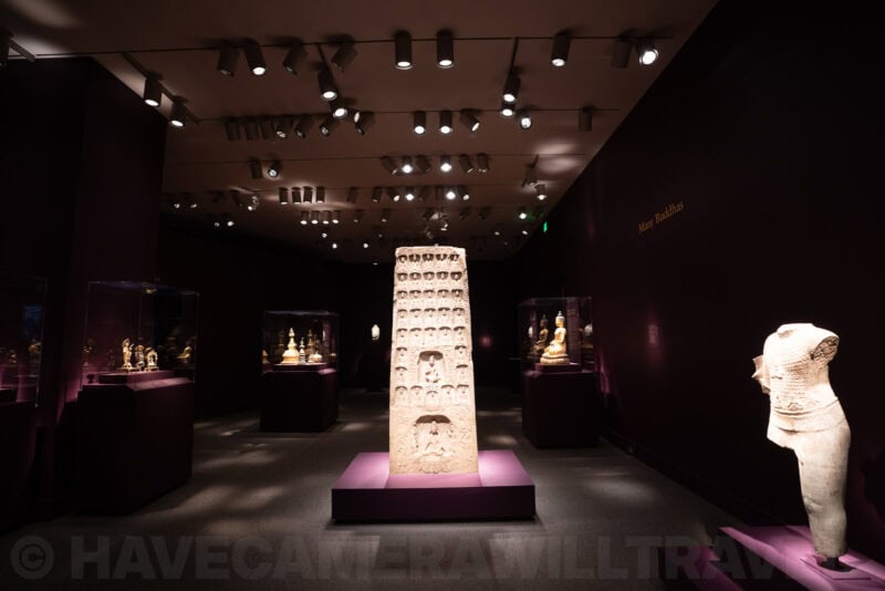 Ancient carved stone stele displayed among museum cases of Buddhist statues in a darkened gallery