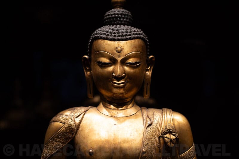 Gilded Buddha statue head and shoulders lit dramatically against a black background