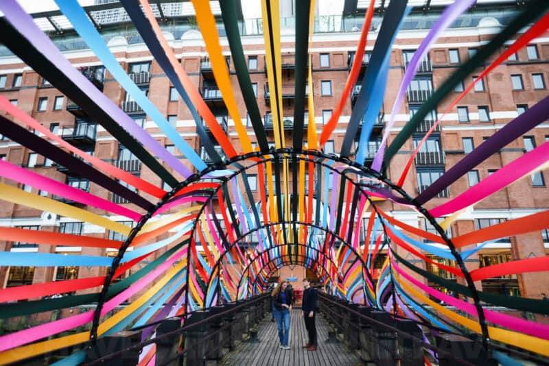 Colorful ribbon-covered arched footbridge with two people standing beneath radiating stripes