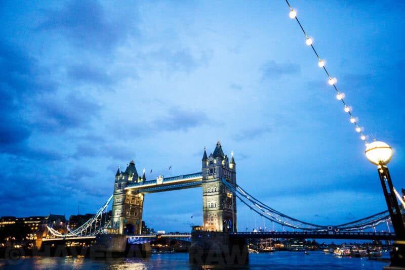 Tower Bridge in London lit up over the Thames at dusk with string lights framing the scene