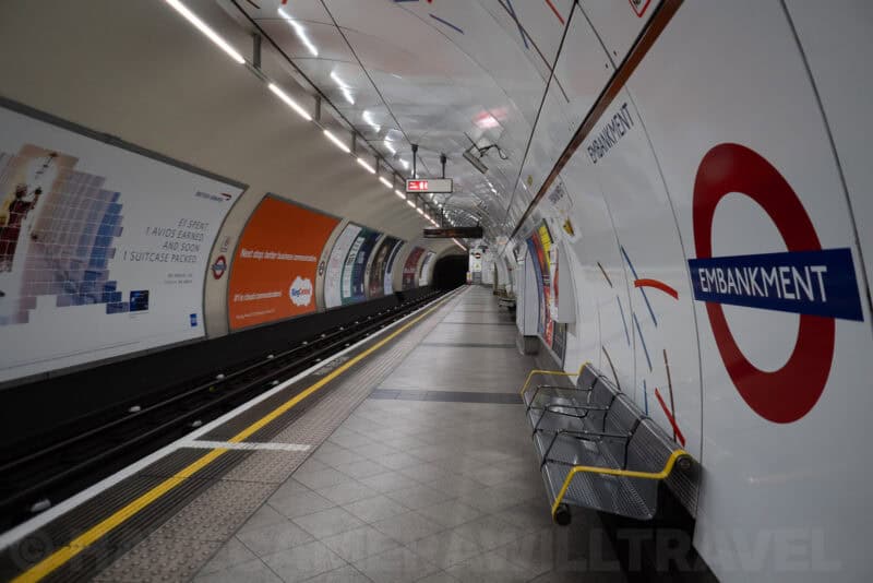 Empty Embankment tube station platform with curved white walls and red roundel sign in London