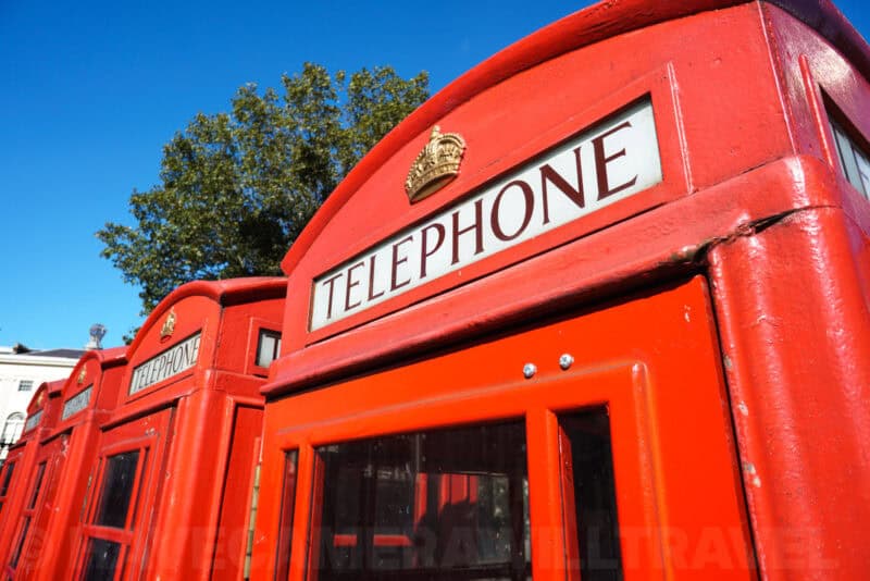 Row of classic red British telephone boxes with crown emblems against a clear blue sky